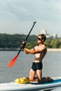 Handsome athletic man with a muscular torso rests on a sup board with an oar in his hands and looks away. A man paddles on the Royalty Free Stock Photo