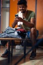 Handsome athletic man sitting in gym locker room, looking at phone, getting ready for workout