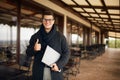 Handsome attractive businessman smiling and showing thumb up sign on office terrace. Stylish man in glasses coat and Royalty Free Stock Photo