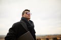 Handsome attractive businessman using a laptop on office terrace. Stylish man in glasses coat and scarf standing on Royalty Free Stock Photo