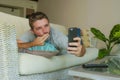 Handsome and attractive happy man sending kiss on internet video call or taking selfie photo with mobile phone lying relaxed at ho Royalty Free Stock Photo