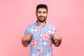 Handsome attractive man with beard and cute smile wearing blue casual shirt, standing pointing at Royalty Free Stock Photo