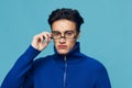 a handsome, attractive man stands on a light blue background in a blue zip-up sweater with black-rimmed glasses turned Royalty Free Stock Photo