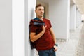 Handsome attractive young man in a stylish red t-shirt in a checkered blue and red vintage shirt in trendy jeans is resting near a