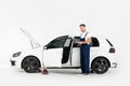 handsome auto mechanic in blue uniform using laptop near broken car