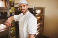 Male baker in uniform leaning on open oven door in bakery beside rack ovens, copy space Royalty Free Stock Photo