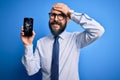 Handsome bald business man with beard holding broken smartphone showing cracked screen stressed with hand on head, shocked with Royalty Free Stock Photo