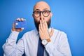 Handsome bald business man with beard holding credit card over isolated blue background cover mouth with hand shocked with shame Royalty Free Stock Photo
