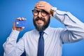 Handsome bald business man with beard holding credit card over isolated blue background stressed with hand on head, shocked with Royalty Free Stock Photo