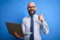 Handsome bald business man with beard working using laptop over blue background happy with big smile doing ok sign, thumb up with Royalty Free Stock Photo