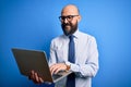 Handsome bald business man with beard working using laptop over blue background with a happy face standing and smiling with a Royalty Free Stock Photo