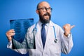 Handsome bald doctor man with beard wearing stethoscope holding chest xray pointing and showing with thumb up to the side with Royalty Free Stock Photo