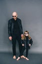 Handsome bald father with his little daughter in black sunglasses and in leather jackets are posing in studio