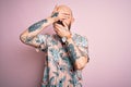 Handsome bald man with beard and tattoo wearing casual floral shirt over pink background Covering eyes and mouth with hands,