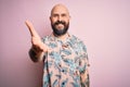 Handsome bald man with beard and tattoo wearing casual floral shirt over pink background smiling friendly offering handshake as