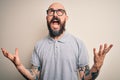 Handsome bald man with beard and tattoo wearing casual polo and glasses crazy and mad shouting and yelling with aggressive