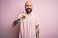 Handsome bald man with beard and tattoo wearing casual shirt over isolated pink background doing happy thumbs up gesture with hand Royalty Free Stock Photo