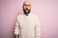 Handsome bald man with beard and tattoo wearing glasses and sweater over pink background making fish face with lips, crazy and Royalty Free Stock Photo