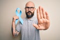 Handsome bald man with beard and tattoos holding blue cancer ribbon over isolated background with open hand doing stop sign with Royalty Free Stock Photo