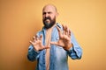 Handsome bald man with beard wearing casual denim jacket and striped t-shirt disgusted expression, displeased and fearful doing