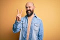 Handsome bald man with beard wearing casual denim jacket and striped t-shirt smiling with happy face winking at the camera doing Royalty Free Stock Photo