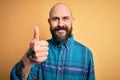 Handsome bald man with beard wearing casual shirt standing over isolated yellow background doing happy thumbs up gesture with hand Royalty Free Stock Photo