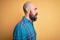 Handsome bald man with beard wearing casual shirt standing over isolated yellow background looking to side, relax profile pose Royalty Free Stock Photo