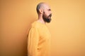 Handsome bald man with beard wearing casual sweater standing over yellow background looking to side, relax profile pose with Royalty Free Stock Photo