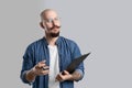 Handsome balded beard with musctache man wearing casual clothes holding clipboard isolated over gray background.