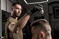 Handsome barber is fixing the styling of brutal young bearded man with a dry styler at a barbershop