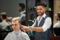 Handsome barber trimming client`s haircut, looking at camera and smiling. Royalty Free Stock Photo
