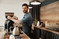 Handsome barista grinds coffee beans in coffeemachine and looks at the camera