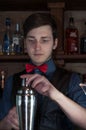 Handsome bartender in blue shirt and red bow tie making drink with sheker