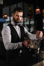 handsome bartender pouring beer from beer taps into glass and looking Royalty Free Stock Photo