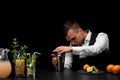 An attractive bartender wipes a shaker, a bar counter with cocktails, limes, lemon and oranges on a black background. Royalty Free Stock Photo