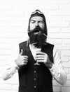 Handsome bearded aviator man with long beard and mustache on funny face holding glass of alcoholic shot in vintage suede Royalty Free Stock Photo