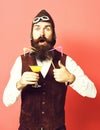 Handsome bearded aviator man with long beard and mustache on surprised face holding glass of alcoholic beverage in Royalty Free Stock Photo