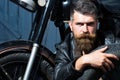 Handsome bearded biker in leather jacket sitting near motorcycle in garage