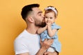 Handsome bearded caring father holding and kissinga little girl, isolated on yellow Royalty Free Stock Photo