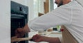 Handsome bearded chef fater in apron taking fresh baked pizza out from oven with circular knife putting on wooden