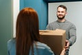 Handsome bearded courier male delivering cardboard box parcel to unrecognizable female customer on doorway at home. Royalty Free Stock Photo