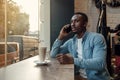 Handsome bearded dark-skinned businessman sitting near cafe window and talks on smartphone with business partner. Royalty Free Stock Photo
