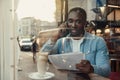 Handsome bearded dark-skinned businessman sitting near cafe window and talks on smartphone with business partner. Royalty Free Stock Photo