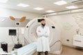 Handsome bearded doctor in medical robe with computed tomograph for obtain detailed internal images of the body of Royalty Free Stock Photo