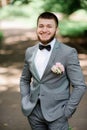 Handsome bearded groom in grey suit with pink boutonniere poses in the park Royalty Free Stock Photo