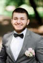 Handsome bearded groom in grey suit with pink boutonniere poses in the park Royalty Free Stock Photo