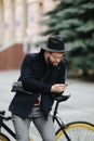 Handsome bearded hipster man using a smart phone and smiling while riding bicycle in city Royalty Free Stock Photo