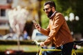 Handsome bearded hipster man is using a smart phone and smiling while riding bicycle in city Royalty Free Stock Photo