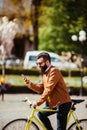 Handsome bearded hipster man is using a smart phone and smiling while riding bicycle in city Royalty Free Stock Photo