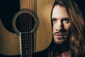 Handsome bearded long haired man holding guitar and looking at camera